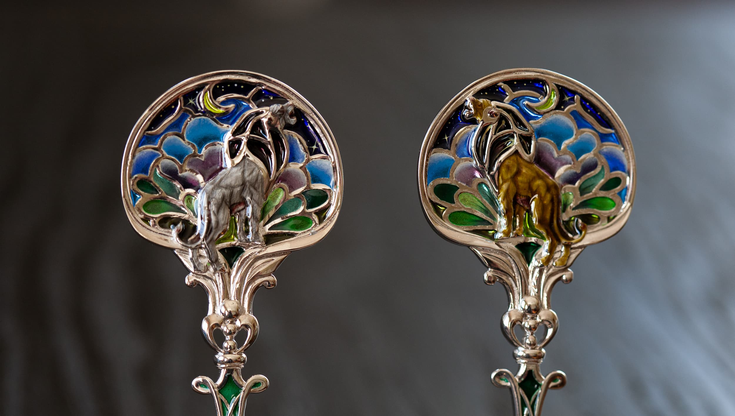 Детальное изображение витражных ложек при дневном свете на темном фоне Серебряная чайная ложка со львом в технике витражной и перегородчатой эмали, изготовленная мастерской Хризолит. Фото 1.