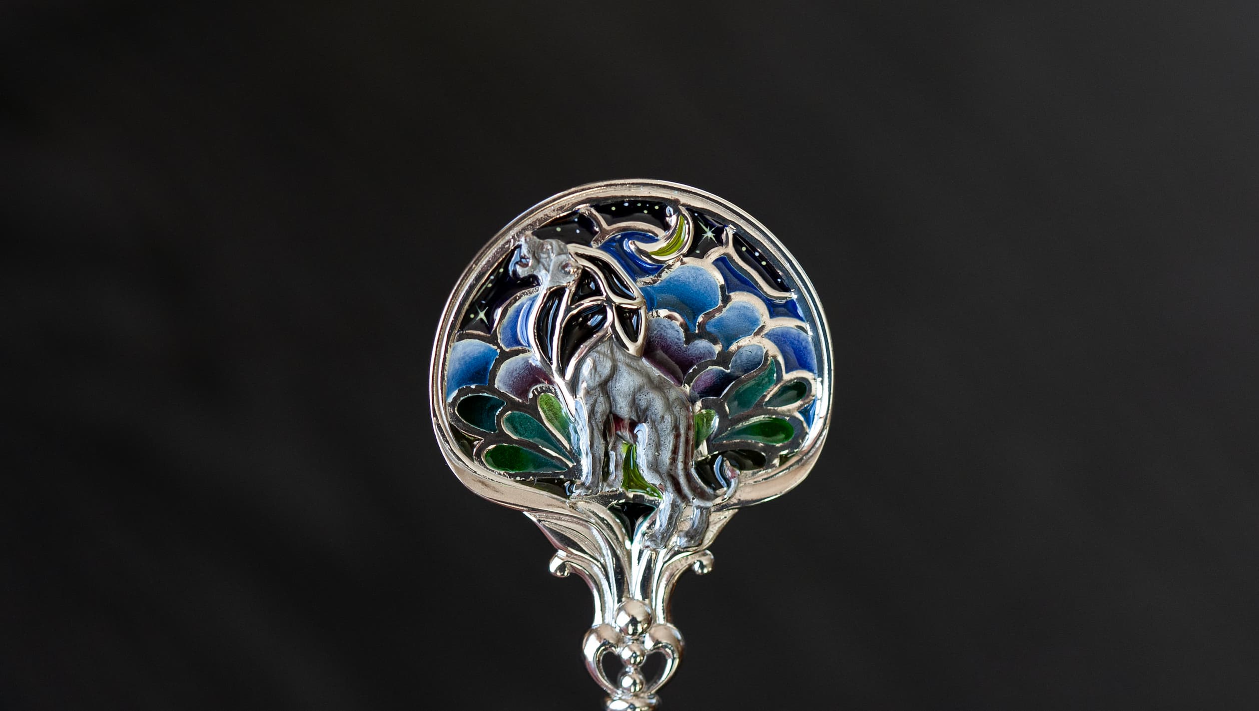 Витражная ложка с серебряным львом на темном неосвещенном фоне Серебряная чайная ложка со львом в технике витражной и перегородчатой эмали, изготовленная мастерской Хризолит. Фото 6.